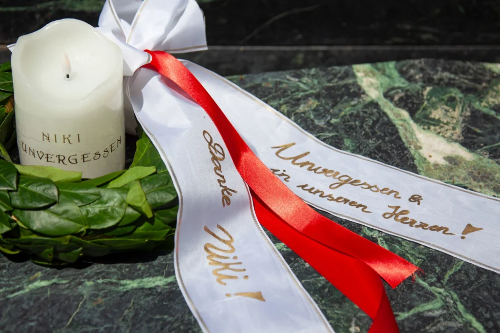 Corona del ganador con pancarta para Niki Lauda con letras doradas y otro lazo rojo